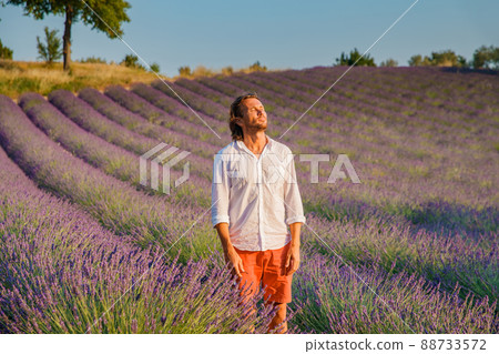 The handsome brutal man with long brunette hair poses in the field of lavender in provence near Valensole, France, clear sunny weather, in a rows of lavender, red shorts, white shirts, blue sky The handsome brutal man with long brunette hair poses in the field of lavender in provence near Valensole, France, clear sunny weather, in a rows of lavender, red shorts, white shirts, blue sky 88733572