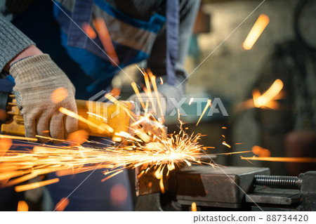 Locksmith in special clothes and goggles works in production. Metal processing with angle grinder. Sparks in metalworking 88734420