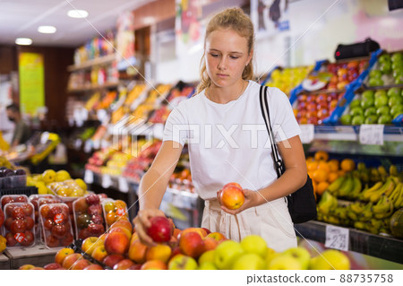 Fifteen-year-old girl chooses apples on the counter 88735758