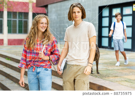 Smiling teenagers boy and girl walking home after finishing college lessons on day 88735975