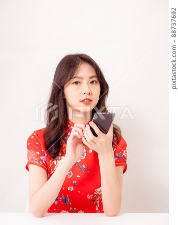 Smiling young asian woman in traditional cheongsam qipao dress using a smart phone isolated on white background. Smiling young asian woman in traditional cheongsam qipao dress using a smart phone isolated on white background. 88737692