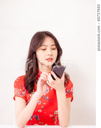 Smiling young asian woman in traditional cheongsam qipao dress using a smart phone isolated on white background. Smiling young asian woman in traditional cheongsam qipao dress using a smart phone isolated on white background. 88737693
