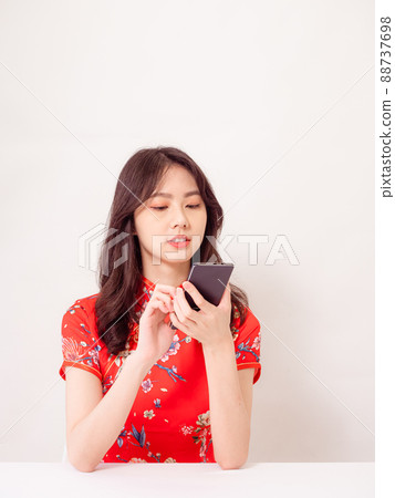 Smiling young asian woman in traditional cheongsam qipao dress using a smart phone isolated on white background. Smiling young asian woman in traditional cheongsam qipao dress using a smart phone isolated on white background. 88737698