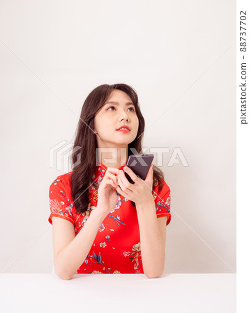 Smiling young asian woman in traditional cheongsam qipao dress using a smart phone isolated on white background. Smiling young asian woman in traditional cheongsam qipao dress using a smart phone isolated on white background. 88737702