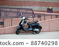 Black motor scooter parked with kick stand in front of handicapped ramp in front of building 88740298