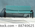 Urban blue metal bench and shadow on sidewalk in front of blue wall 88740625
