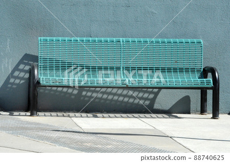 Urban blue metal bench and shadow on sidewalk in front of blue wall Urban blue metal bench and shadow on sidewalk in front of blue wall 88740625