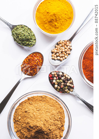 Variety of spices and herbs in spoons and bowls on white background, top view, vertical format. Cooking ingredients and condiments concept. Variety of spices and herbs in spoons and bowls on white background, top view, vertical format. Cooking ingredients and condiments concept. 88742015