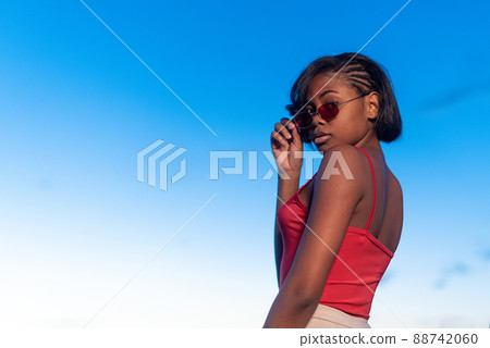 Black young woman posing confident holding a sunglasses during dusk Black young woman posing confident holding a sunglasses during dusk 88742060