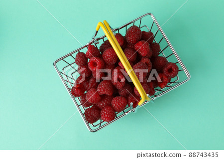 Red juicy raspberries in a shopping basket on a menthol background 88743435