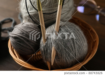 Wicker bowl with yarn balls and knitting needles, and glasses on wooden background 88743826