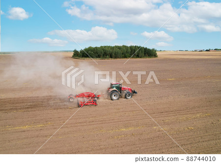 Field cultivating, aerial view. Tractor with disk harrow on plowed.  88744010