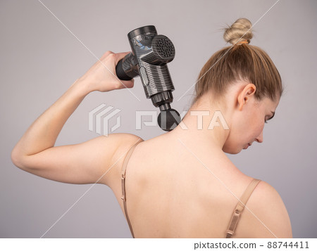 Caucasian woman giving herself a back massage with a gun.  88744411