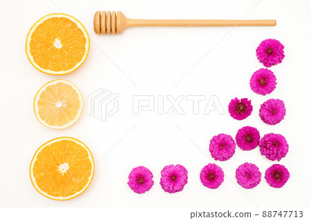 A flat lay of slices of orange fruit with red orchid petals and a wooden honey spoon lying on white background, copy space 88747713