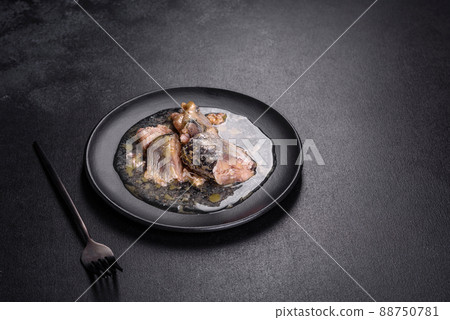Canned sardine in oil on a black round plate against a dark concrete background 88750781