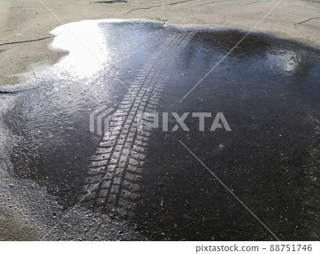 Track from a studded tire on the ice of a frozen puddle on cracked asphalt in the bright sunshine on a winter day 88751746