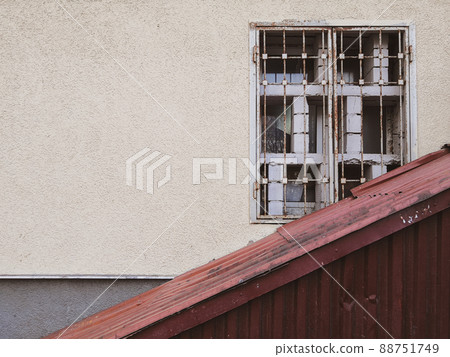 A yellow wall on which an old dirty window with a metal grill is obliquely closed with corrugated rusty iron. A yellow wall on which an old dirty window with a metal grill is obliquely closed with corrugated rusty iron. 88751749