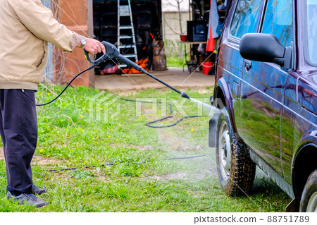 A gray-haired elderly man washes a car outdoors with a high-pressure apparatus. A gray-haired elderly man washes a car outdoors with a high-pressure apparatus. 88751789