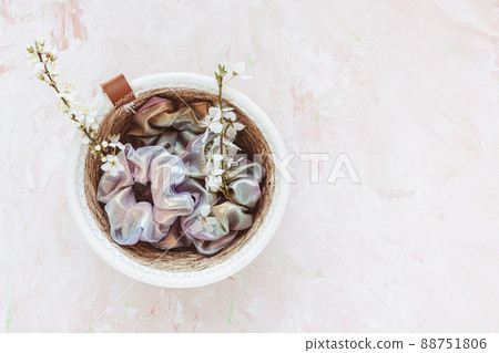 Trendy holographic shiny scrunchies in basket for accessories and white spring flowers, copy space 88751806