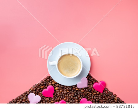 White cup with coffee and silk hearts on coffee beans on a pink background. White cup with coffee and silk hearts on coffee beans on a pink background. 88751813