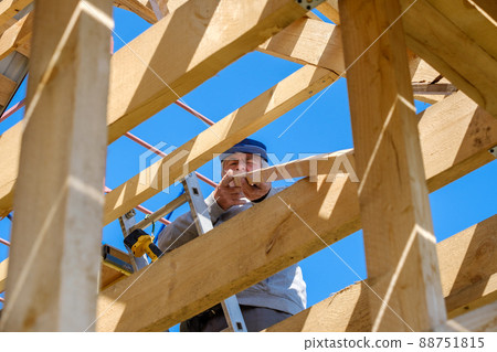 Senior gray-haired builder collects the frame of a wooden country house Senior gray-haired builder collects the frame of a wooden country house 88751815