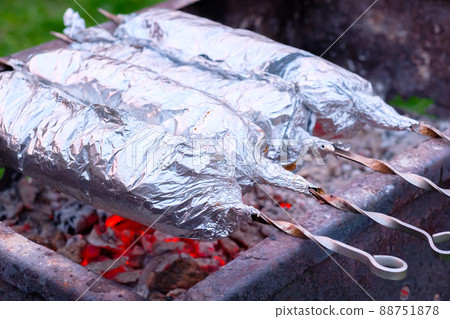 The meat on metal skewers is wrapped in aluminum foil and grilled on charcoal. 88751878