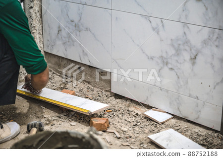 Male tiler using trowel laying marble tile with cement in bathroom. Housing development, improvement renovation 88752188
