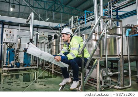 Caucasian technician engineer man sitting and holding blueprint of industrial project with boiler and pipeline in beverage processing plant 88752200