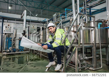 Caucasian technician engineer man sitting and holding blueprint of industrial project with boiler and pipeline in beverage processing plant 88752201