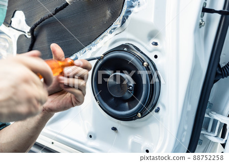 Mechanic using screwdriver screwing drywall screw with car speaker on vehicle door 88752258