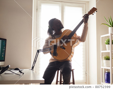 Young man is singing and playing guitar while making an audio recording at home Young man is singing and playing guitar while making an audio recording at home 88752399