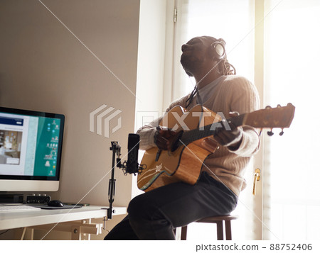 Young man is singing and playing guitar while making an audio recording at home Young man is singing and playing guitar while making an audio recording at home 88752406
