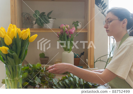 Confident woman florist in glasses and an apron works at the workplace with flowers. Creation of a composition of fresh eucalyptus 88752499
