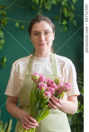 Successful young woman - small business owner. Professional florist with a beautiful bouquet of fresh flowers in the store looks into the camera 88752500