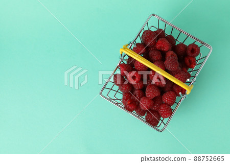 Red juicy raspberries in a shopping basket on a menthol background 88752665
