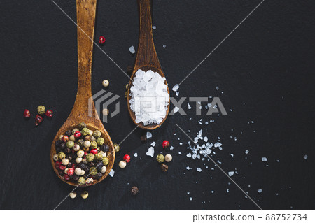 Wooden spoons with pepper and salt on a blackboard base, top view with copy space. Cooking ingredients and condiments concept. 88752734