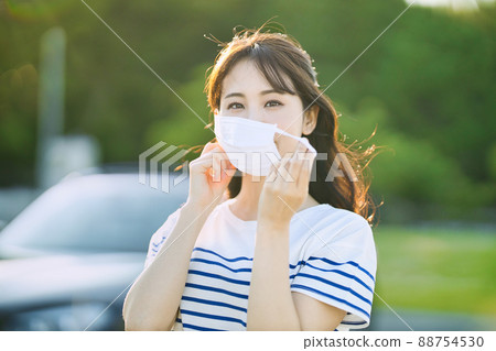 A smiling young woman taking off her mask outdoors 88754530