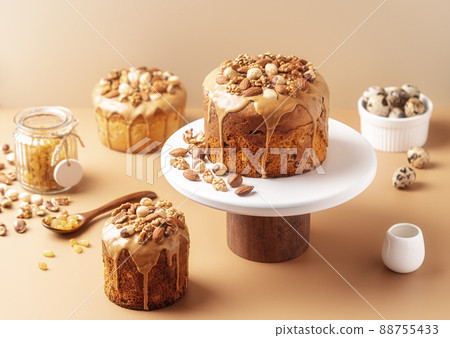 Caramel glazed Easter cakes decorated with nuts on pastel background. Easter composition with cakes, nuts, raisins and quail eggs. Easter background with copy space for your design. Caramel glazed Easter cakes decorated with nuts on pastel background. Easter composition with cakes, nuts, raisins and quail eggs. Easter background with copy space for your design. 88755433