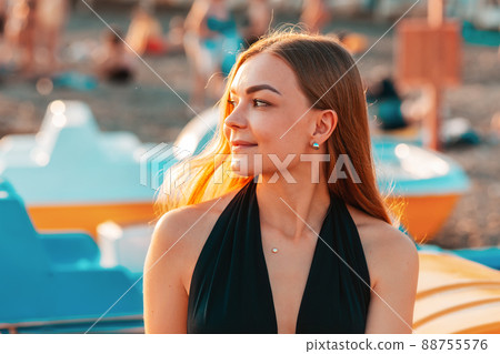 Portrait of a young beautiful blonde smiling woman in the sun. In the background, the beach is in a blur Portrait of a young beautiful blonde smiling woman in the sun. In the background, the beach is in a blur 88755576