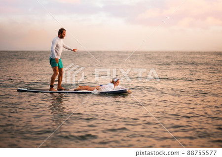 Happy father and daughter surfing on a sup board and have a funny time. Sunset ocean at the background. Family summer vacations Happy father and daughter surfing on a sup board and have a funny time. Sunset ocean at the background. Family summer vacations 88755577
