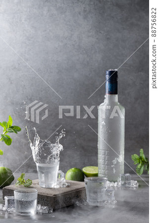 Bottle of vodka with splash shot glass on concrete background with copyspace.. Vertical format. Bottle of vodka with splash shot glass on concrete background with copyspace.. Vertical format. 88756822