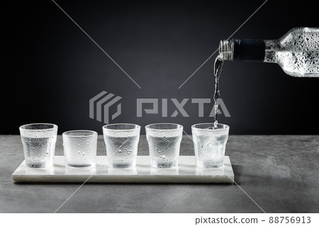 Pouring cold vodka into shot glass isolated on dark background. Selective focus. Pouring cold vodka into shot glass isolated on dark background. Selective focus. 88756913