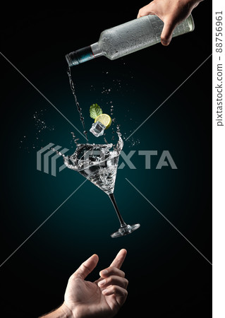 Mans hand support flying glass of cocktail drink with splash on dark blue background. Gravity concept. 88756961