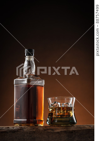 Bottle of whisky and glass of whisky with ice on wooden log with orange and black degraded background, with copy space. 88757499