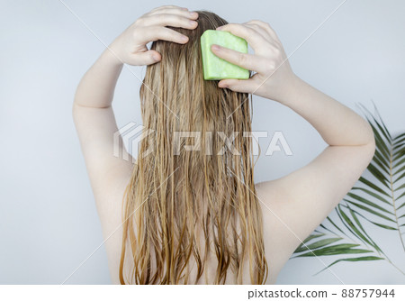 Solid hair shampoo. Close-up of a blonde girl in the bathroom, which lathers her hair with dry shampoo. Lots of foam and peek effect. Solid hair shampoo. Close-up of a blonde girl in the bathroom, which lathers her hair with dry shampoo. Lots of foam and peek effect. 88757944