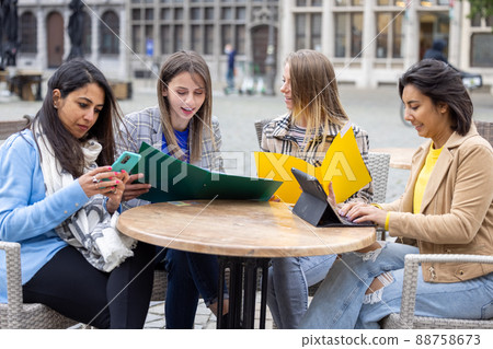 Diverse group of young business woman discussing something on a laptop in a bar courtyard after work Diverse group of young business woman discussing something on a laptop in a bar courtyard after work 88758673