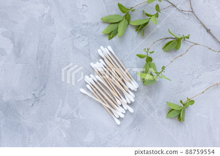 Eco-friendly bamboo cotton buds on gray background, green leaves. Cotton swabs, ear cleaner sticks. 88759554