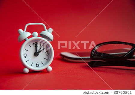 Alarm clock pointing at 2 o'clock with glasses and phone background. Copy space concept Alarm clock pointing at 2 o'clock with glasses and phone background. Copy space concept 88760891