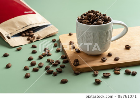 Roasted coffee beans in a small white cup on a pastel green background. Roasted coffee beans in a small white cup on a pastel green background. 88761071