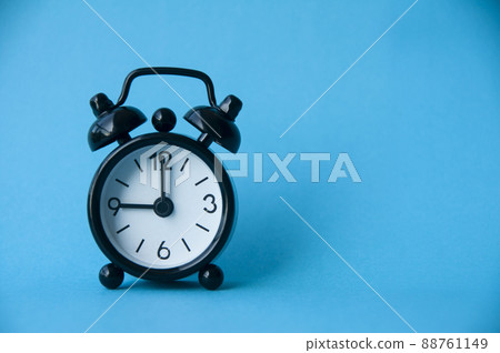 Black alarm clock isolated on light blue background. The clock set at 9 o'clock. 88761149